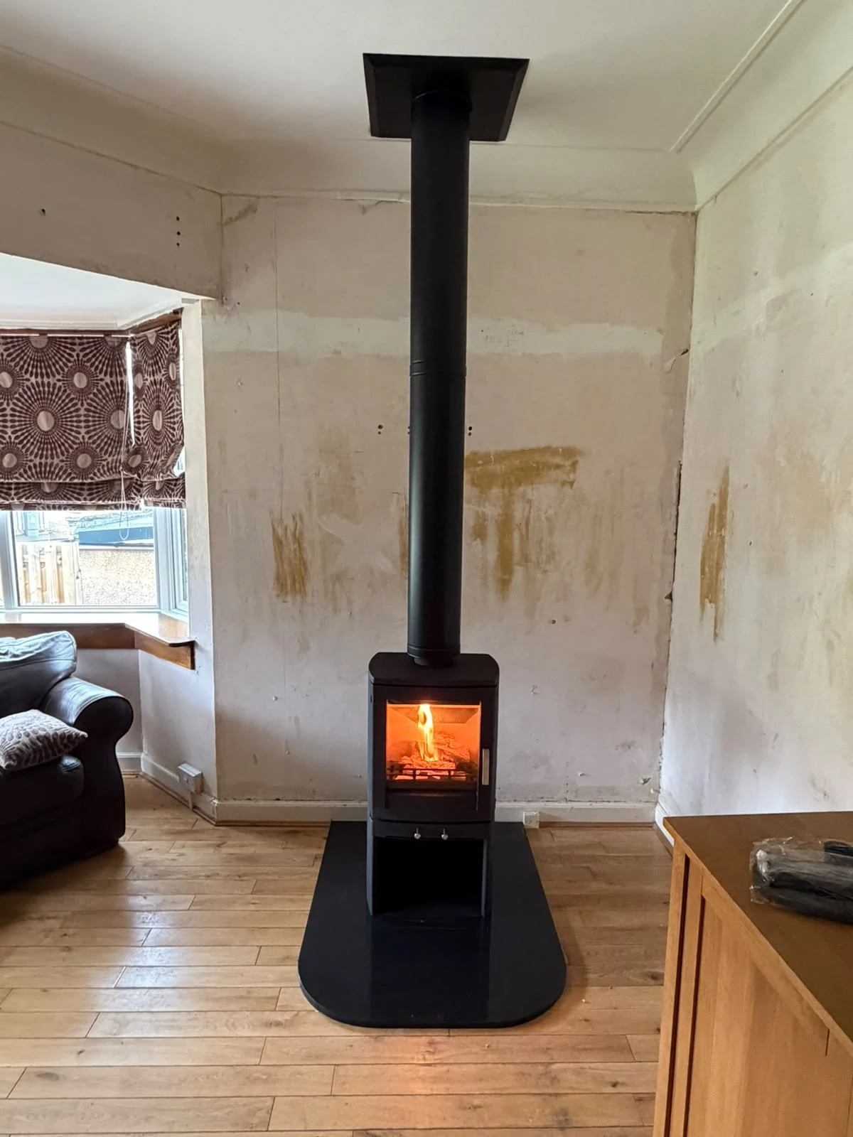 Lit freestanding stove with a tall black flue and rounded hearth