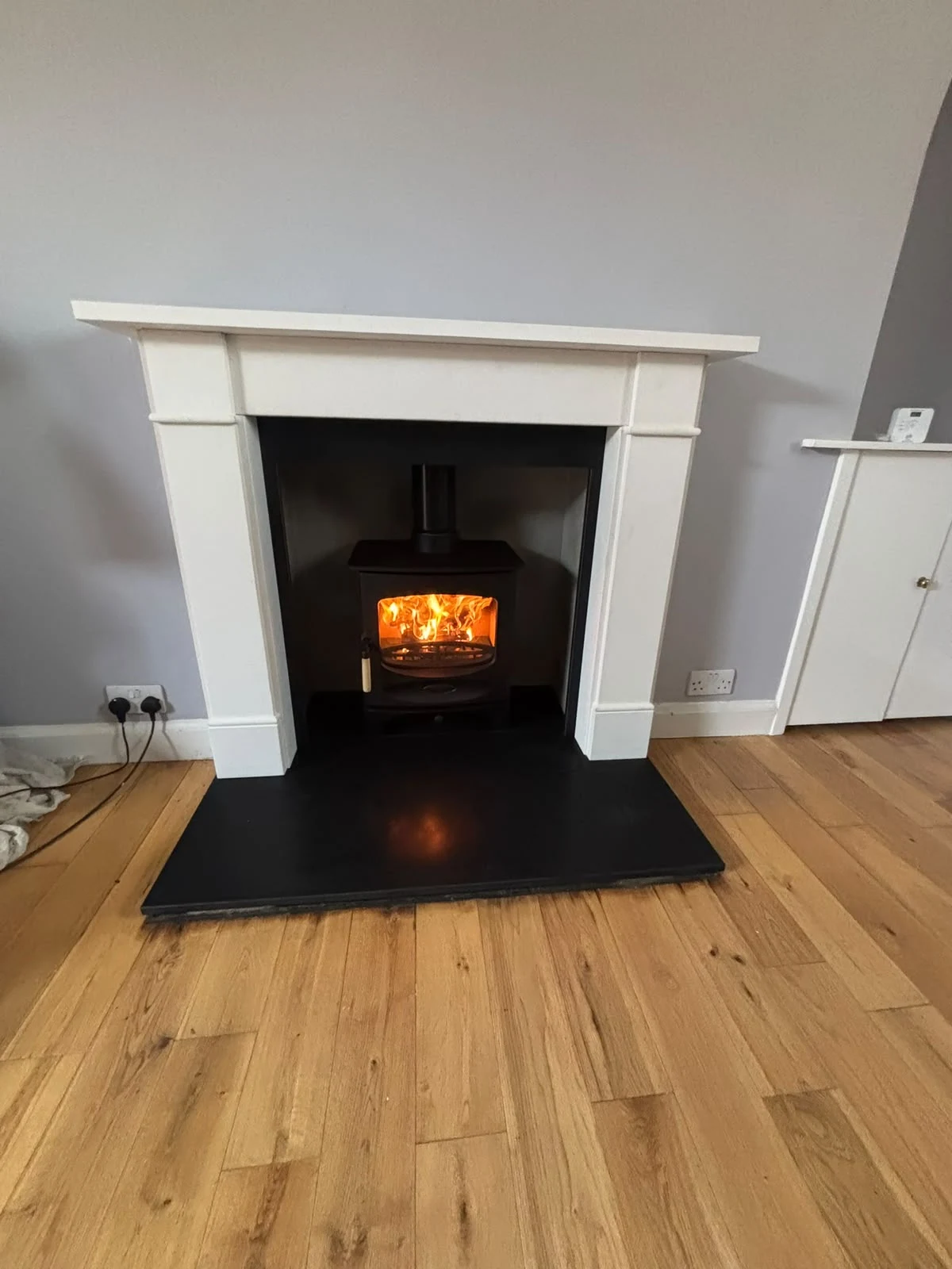 Completed stove installation with a white fireplace, black hearth and finished timber floor