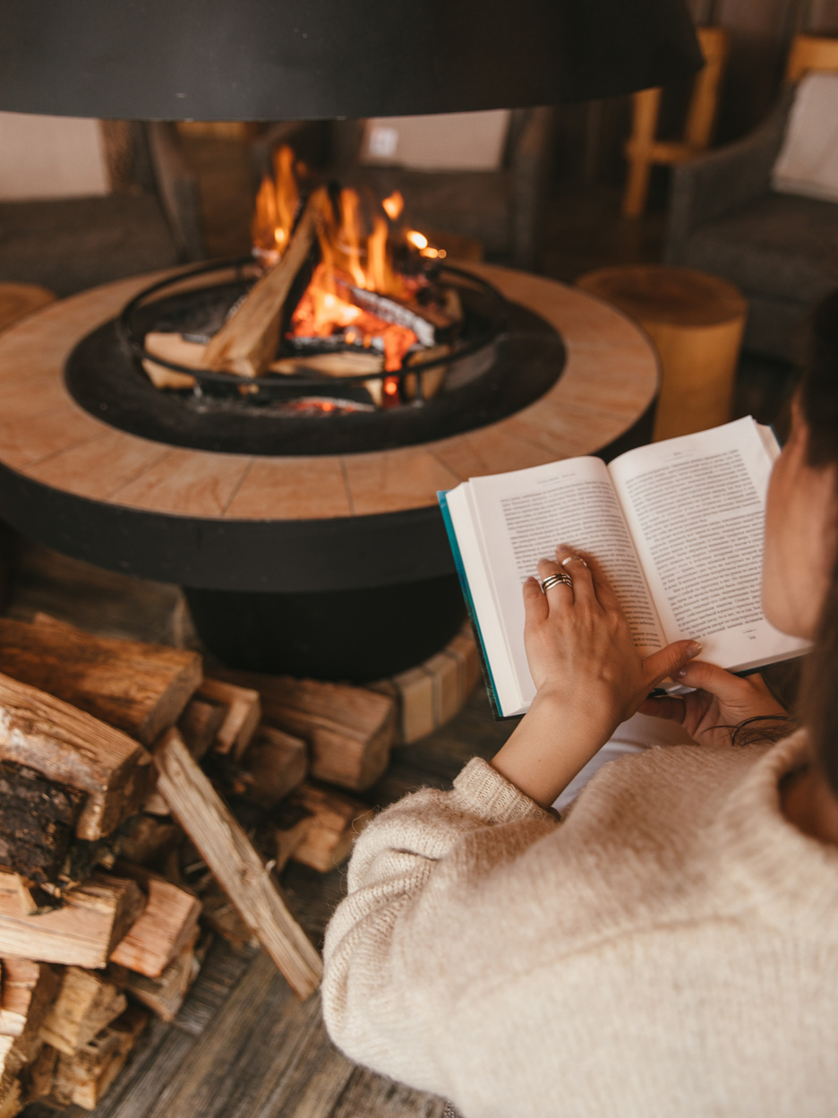 A Person Reading a Book Near the Fireplace