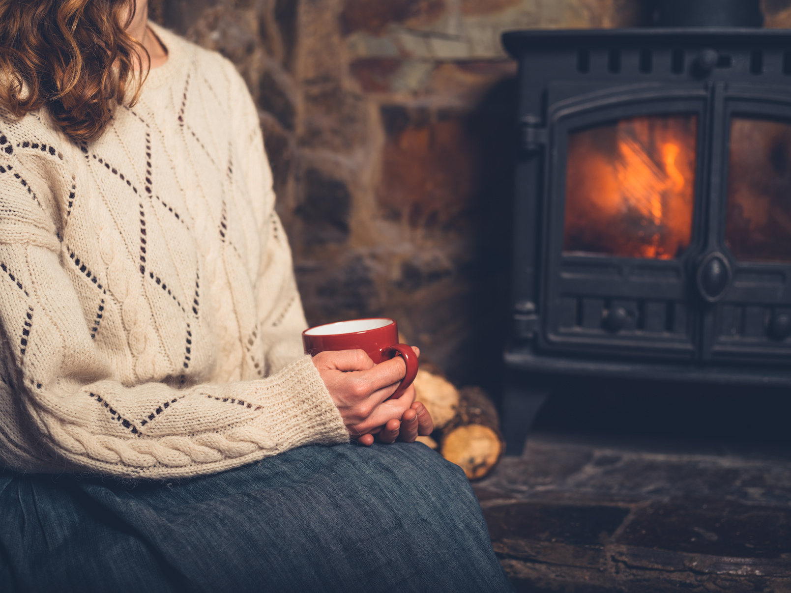 Woman in White Jumper by Fireplace with Mug